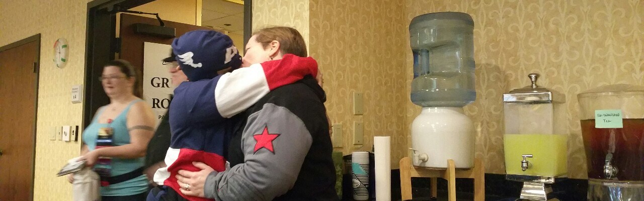 Two women, one in a Captain America hoodie, one in a Winter Soldier hoodie, kissing.